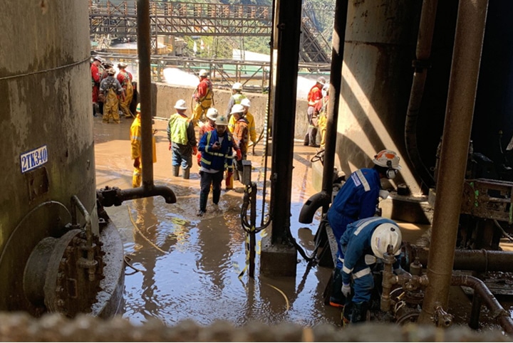 Industrial workers wearing safety gear assess flood damage in a waterlogged facility, inspecting equipment and infrastructure in a manufacturing plant.