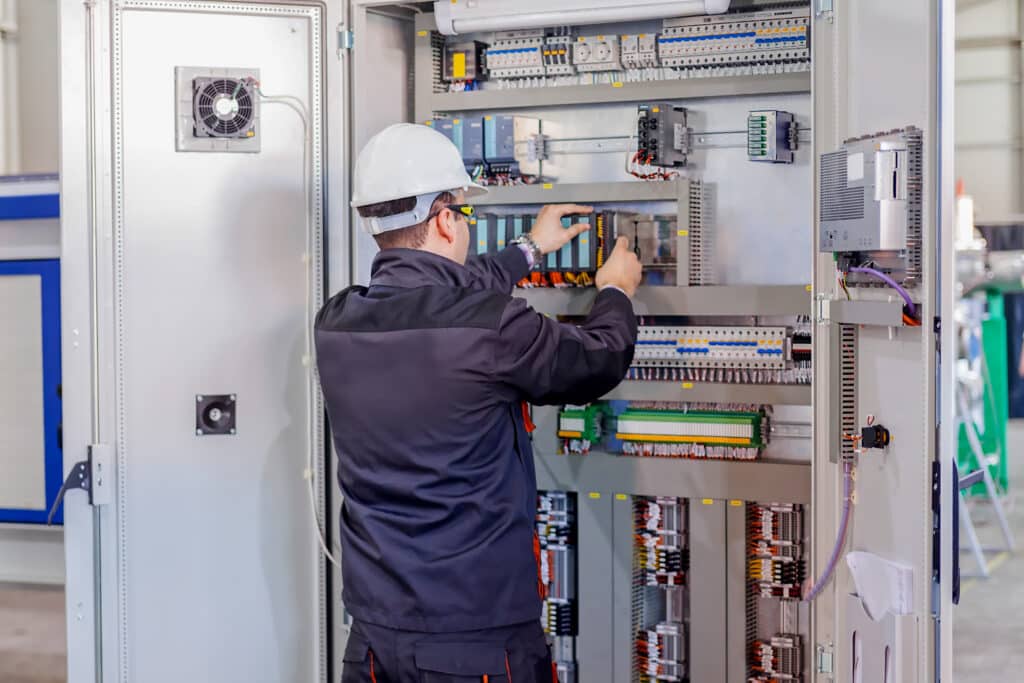 ManWorkerCheckingAdvancedIndustrialControlPanelNoteShallowDepth - Avid Solutions